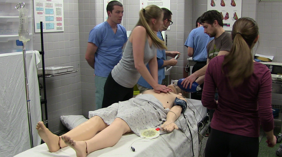 Medical students practice emergency resuscitation techniques on a patient mannequin during a simulation.